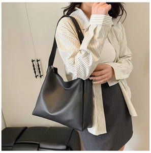 Close-up of a black matte leather tote bag with wide shoulder strap on model