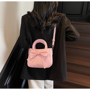 Pink bucket bag with large bow detail shown carried by model against a retro backdrop