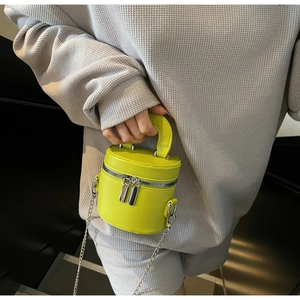 Detail of lime yellow cylindrical bucket bag with dual zippers and silver chain strap
