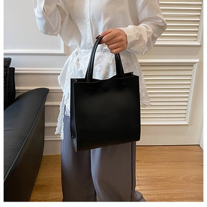 Detail of minimalist black matte leather tote bag held by a model in a modern room