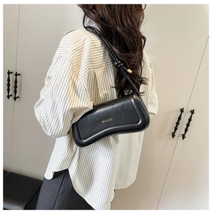 Detail of minimalist black leather shoulder bag with curved base and gold logo on the side