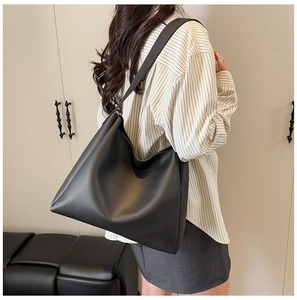Detail view of a large black matte leather tote bag worn on shoulder for daily commute