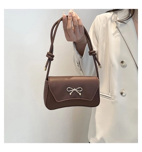 Close-up of brown shoulder bag featuring golden bow metal buckle and knotted strap detail