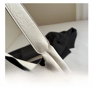 Close-up of the smooth leather texture and strap stitching on a creamy white tote bag