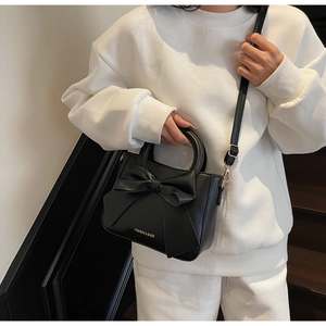 Détail du sac seau noir avec grand nœud décoratif et poignée anneau en métal doré