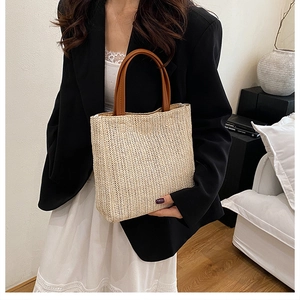 Close-up of woven straw tote bag with brown leather handles and fine texture