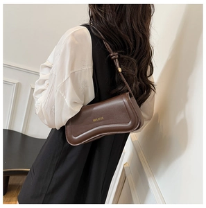 Detail of a brown leather shoulder bag featuring a gold brand logo and adjustable strap