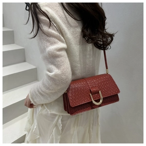 Détail du sac bandoulière rouge tressé avec boucle fer à cheval dorée porté par un mannequin