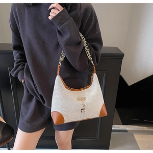 Detail of off-white tote bag with brown leather trim and golden deer pendant accent
