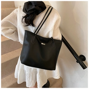 Détail d'un sac cabas en cuir grainé noir avec plaque logo argentée sur la bandoulière