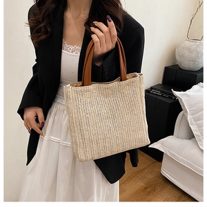 Detailed herringbone weave texture on a beige straw tote bag with brown leather handles