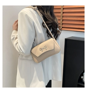 Detail of beige shoulder bag with metallic bow showing leather texture and sleek side profile