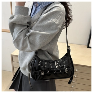 Detail of black glossy Y2K shoulder bag with silver eyelets and buckle straps