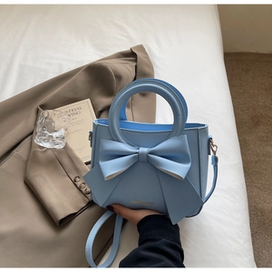 Close-up of light blue handbag featuring a large bow and gold logo on a white bed