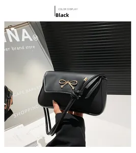 Detail of a black leather baguette bag featuring a gold metal bow on the front flap