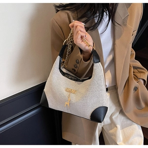 Detail of beige woven tote bag with black leather corners and gold deer charm detail
