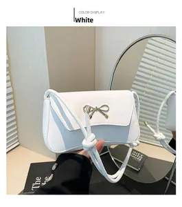 Detailed view of white faux leather bag with a golden metal bow and elegant knotted strap