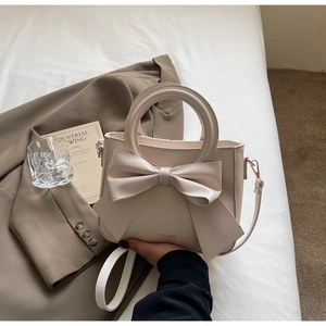 Detail of cream white PU handbag featuring a large bow design and gold ring handle