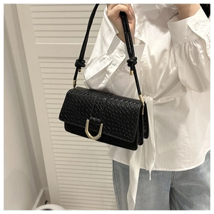 Detail of woven texture on black shoulder bag with prominent gold U-shaped hardware buckle