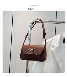 Detail of a brown leather underarm bag featuring a delicate metal bow clasp buckle