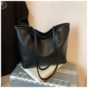 Close-up of black litchi grain leather tote bag featuring a metallic logo plate detail