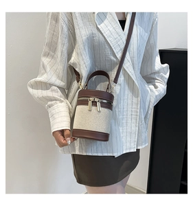 Detail of minimalist bucket bag with cream canvas, brown leather trim and gold zippers