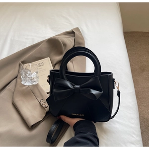 Detail of black faux leather handbag with oversized bow decor and gold hardware accents