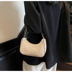 Detail of cream straw crescent bag featuring thick gold chain strap on shoulder