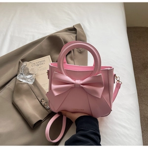 Detail of pink bow handbag featuring PU leather texture and a circular metal handle