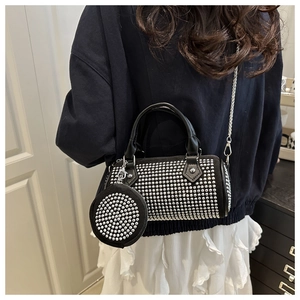 Close-up of black cylinder bag with silver studs, leather handle and metal chain strap