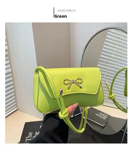 Detail of a bright green leather baguette bag with a metallic bow and knotted strap