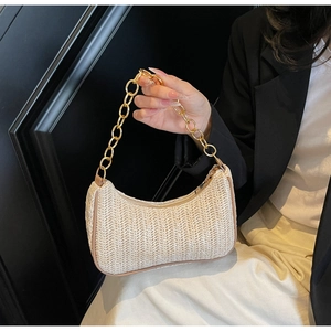 Detail of woven straw shoulder bag featuring thick gold chain and brown piping