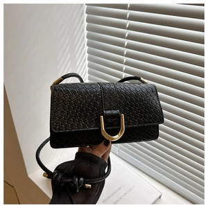 Détail d'un sac noir à texture crocodile avec boucle en U dorée et bandoulière tressée