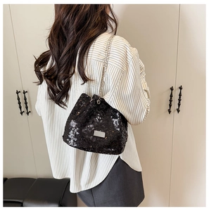 Detail of a chic black sequined bucket bag with silver chain strap on model shoulder