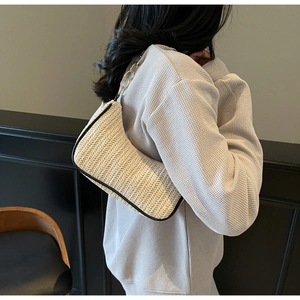 Detail of beige straw crescent bag with gold chain strap and black trim texture