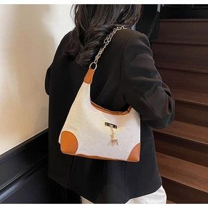 Detail of canvas tote with brown leather trim and golden deer charm on shoulder bag