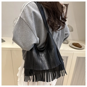 Close-up of black leather shoulder bag featuring long fringe tassels and premium texture