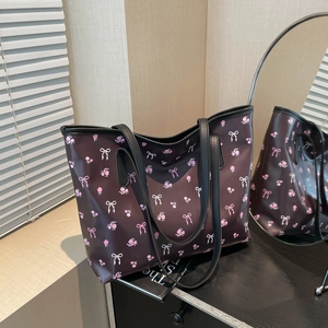 Floral print tote bag with pink bows and black straps on a dark wooden surface