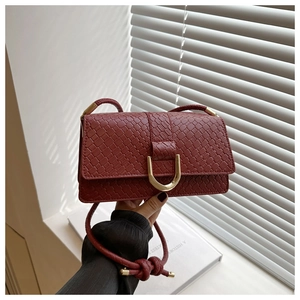 Détail du sac bandoulière tissé bordeaux avec boucle en U dorée et texture raffinée