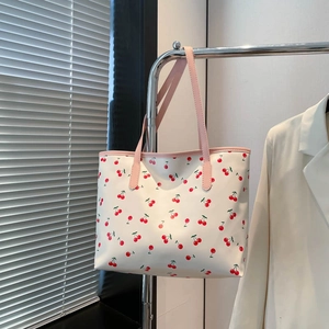 White tote bag with cherry print and pink handles hanging in a bright casual setting