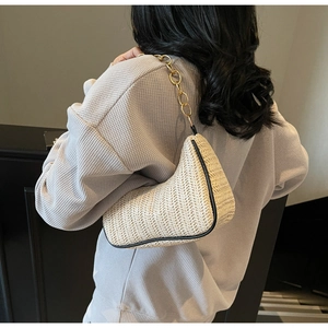 Detailed texture of beige woven shoulder bag with black piping and gold chain strap
