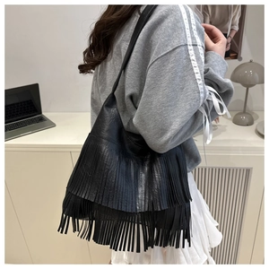 Detail of bohemian black tote bag featuring long fringes shown on a model's shoulder