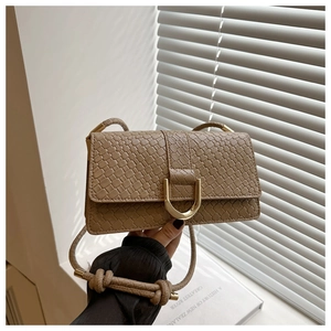 Détail d'un sac tressé avec boucle en fer à cheval dorée et bandoulière à nœuds