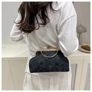 Détail de broderie papillon sur petit sac de soirée en velours noir avec poignée dorée