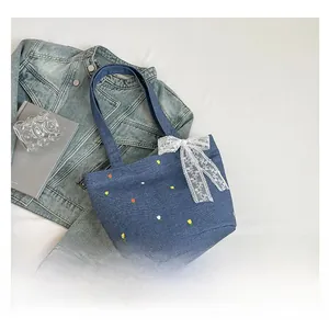 Detail of blue denim tote bag with colorful tulip embroidery and white lace bow