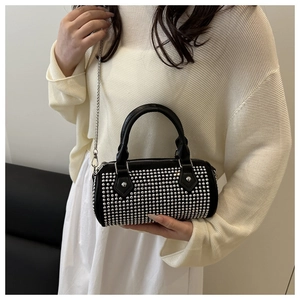 Detail of black cylinder bag with silver studs and metal chain on white knitwear