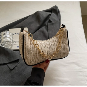 Close-up of beige woven crescent bag featuring bold gold chain and black trim accents