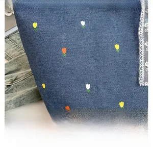 Close-up of denim tote bag featuring tulip embroidery and white lace border detail