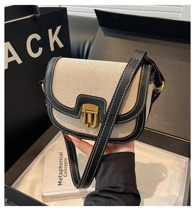 Detail of canvas and leather crossbody saddle bag with gold hardware and contrast stitching