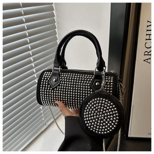 Detail of black cylinder bag with silver studs, metal chain, and round coin purse charm